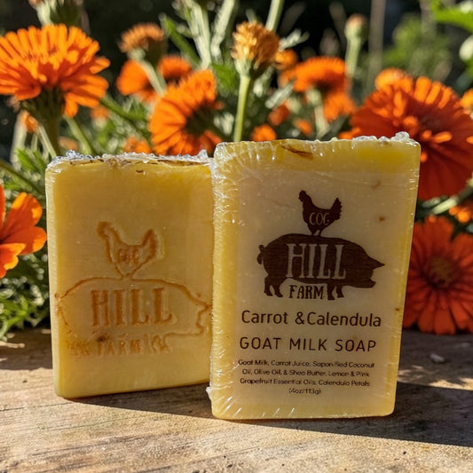 Two bars of Hill Farm soap with carrot and calendula on a wooden surface with orange flowers in the background.